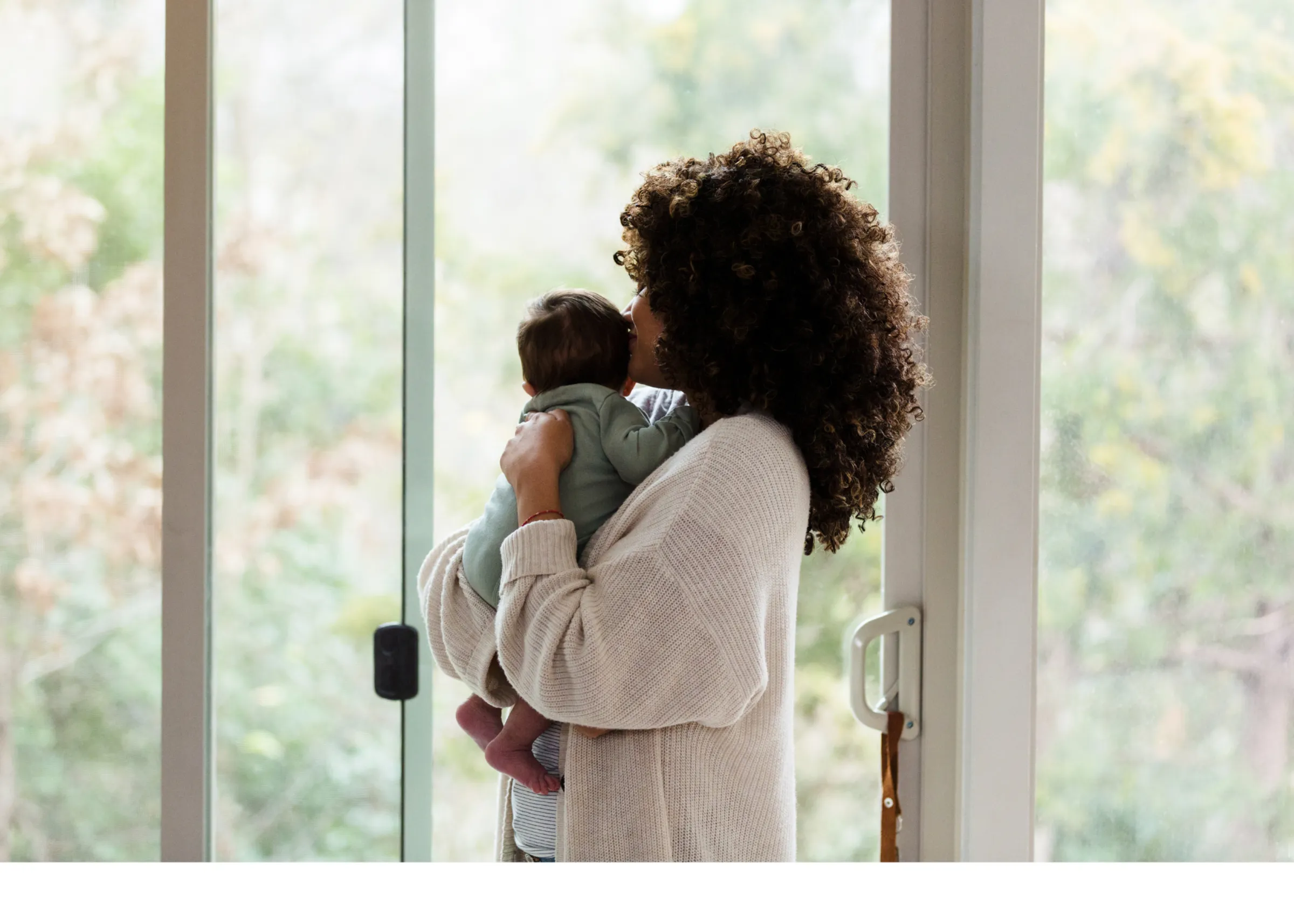 Mother kissing her baby in front of a bright window